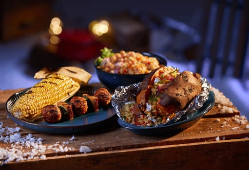 Plate with tasty grilled corn with meatballs on skewer near bowl of sweet potato with bulgur on wooden table under snow