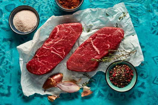 Top view of uncooked beef strip steak served with salt and pepper with spices on parchment