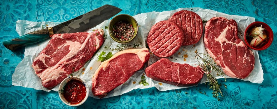 Top view of raw burger patties with ribeye and sirloin steaks with spices and knife on creased paper