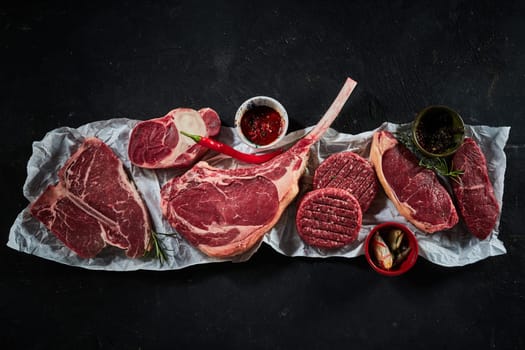 Top view of assorted raw beef steaks including t bone tomahawk sirloin served with different spices and chili pepper and rosemary twigs