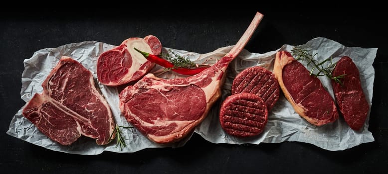 Top view of uncooked tomahawk t bone and sirloin beef steaks garnished with rosemary sprigs and chili pepper