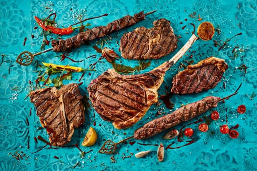 Top view of delicious grilled meat steaks with tomatoes and seasonings placed on blue table