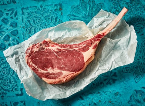 Top view of raw tomahawk beef steak on creased paper on table with ornament