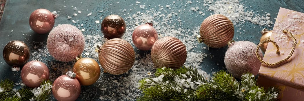 From above of assorted shiny Christmas baubles and gift bag placed with decorative spruce branches on black table with artificial snow