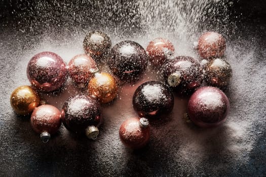 Top view of various shiny Christmas balls on black table being poured with white decorative snow