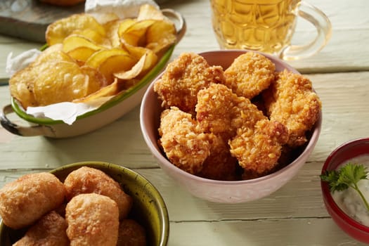 From above of tasty deep fried chicken pieces against croquettes and potato chips with mug of beer and sauce