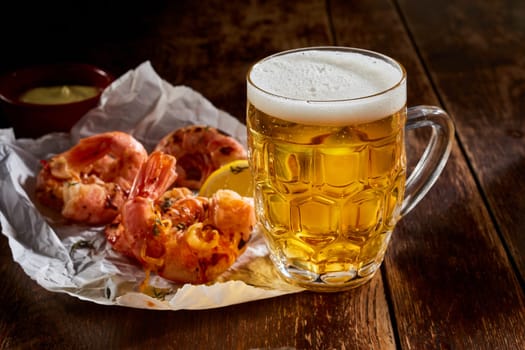 Delicious spicy grilled pink prawns with a cold mug of beer served on crumpled paper on a rustic bar counter with copyspace for menu advertising