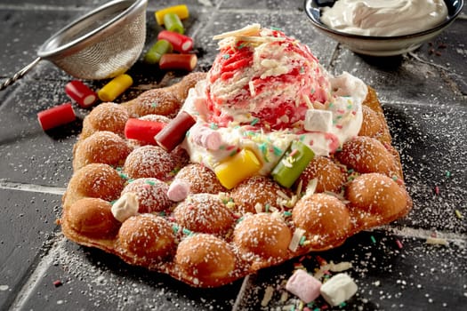 Party treat with bubble waffle and candy dessert topped with whipped cream and a scoop of fruity variegated ice-cream in a high angle view for menu advertising