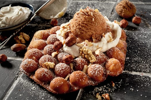 Traditional bubble waffle with nutty ice-cream and fresh walnuts or pecan nuts and hazelnuts on whipped cream sprinkled with sugar in a high angle close up for menu advertising
