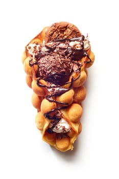Top view of egg waffle cone with ice cream and chocolate with cookie and syrup on white surface