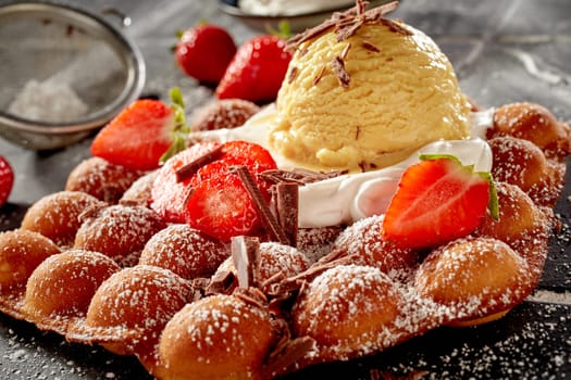 Traditional egg waffle or bubble waffle topped with fresh strawberries, whipped cream and a scoop of vanilla ice-cream topped with chocolate shavings in close up for menu advertising