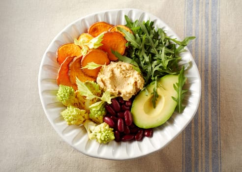 Top view of Buddha bowl with appetizing various vegetables and hummus placed on table for vegetarian lunch