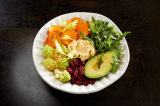 From above of vegetarian Buddha bowl with fresh assorted vegetables and hummus served on black table for healthy lunch
