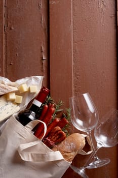 Top view of baguette and bottle of red wine placed on wooden table with wineglasses and cheese
