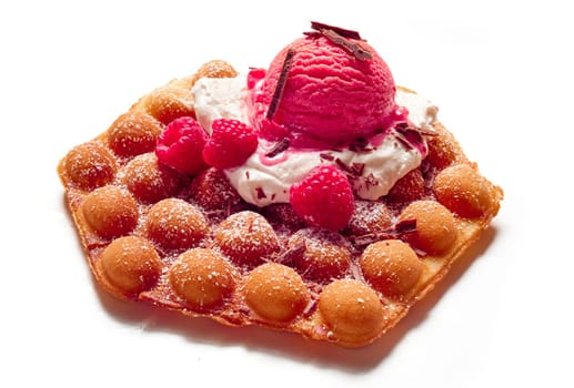 High angle of yummy sweet bubble wafer with ice cream scoop and fresh raspberries sprinkled with grated chocolate on white background in studio