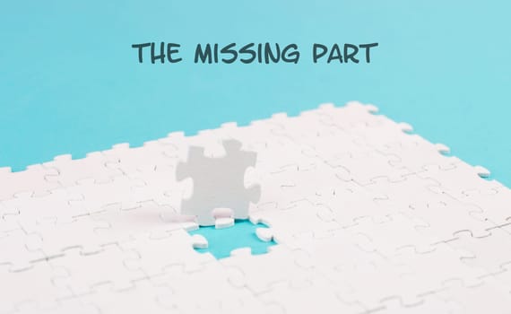White jigsaw on a blue background, the missing part is standing on the paper, working together as a team, searching for solutions, the last piece