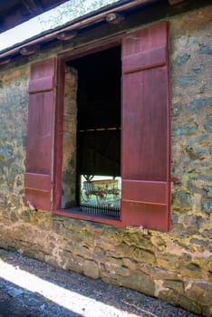 Beautiful colonial Pennsylvania stone barn with large open window and red shutters. Large wooden antique wagon seen through opening. Excellent historical image in natural light with no people and copy space.