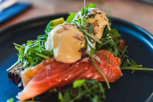 Selective focus on breakfast on the plate. Eggs benedict with salmon, arugula with sunflower seeds