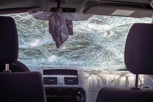 Broken windshield of a car from a bullet, from a shot from a firearm, view from the inside of the cabin. Damaged glass with traces of an oncoming stone on the road. Interior view of the car