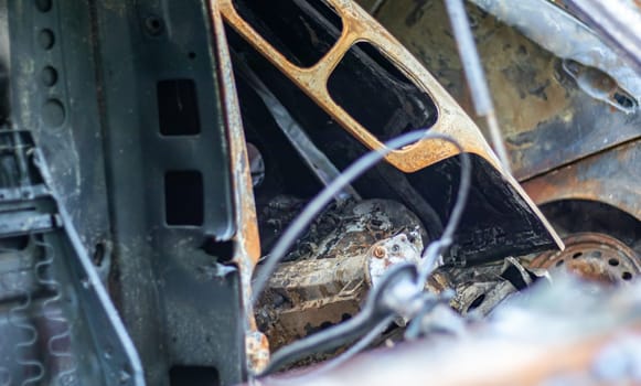 The car was completely destroyed by fire. Abandoned, burnt and rusty car by the road. Cars were on fire in the parking lot. War of Russia against Ukraine. Shrapnel and bullet holes in cars