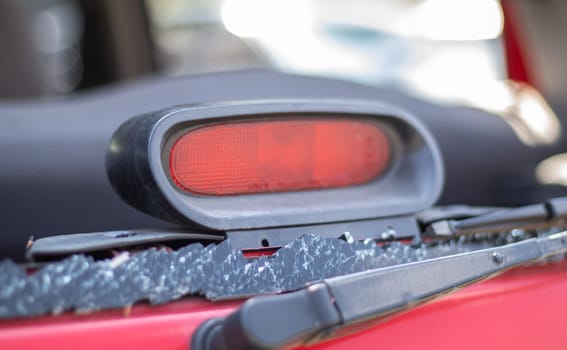 A car after an accident with a broken rear window. Broken window in a vehicle with a rear brake light. Interior wreckage, detailed close-up view of a damaged modern car