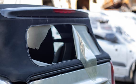 Damaged roof material on the back of the convertible. Vandalism, thieves cut the roof of a convertible from behind. Theft of things from the car. Criminal incident. Car burglary