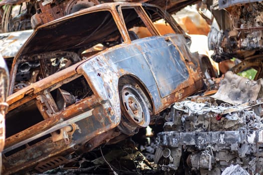 Cars after the fire. Iron parts of a burnt car. Burnt-out cars abandoned on the side of a quiet countryside. Explosion, the result of a fire. Car insurance concept. War of Russia against Ukraine