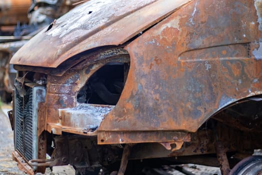 The car was completely destroyed by fire. Abandoned, burnt and rusty car by the road. Cars were on fire in the parking lot. War of Russia against Ukraine. Shrapnel and bullet holes in cars
