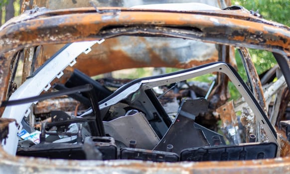 The car burned down completely, even the tires burned out. Burnt out car crash after fire. The bomb shell of the terrorist attack blew up civilians. Disaster zone. Abandoned car on the road
