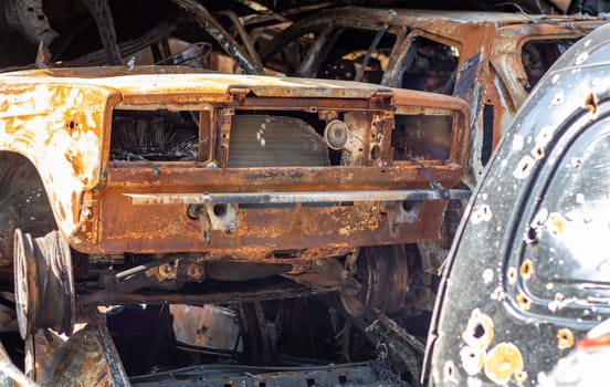 The car burned down completely, even the tires burned out. Burnt out car crash after fire. The bomb shell of the terrorist attack blew up civilians. Disaster zone. Abandoned car on the road