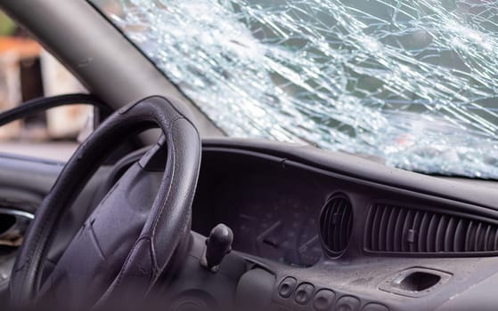 Close-up of the steering wheel of a car after an accident. The driver's airbags did not deploy. Soft focus. Broken windshield with steering wheel. Vehicle interior. Black dashboard and steering wheel