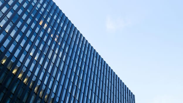 Modern high-rise building against the blue sky. Bottom view of a skyscraper in the business district. Low angle view of the glass facade of an office building