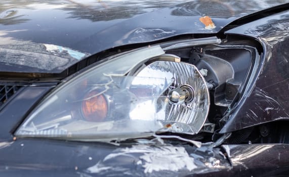 Broken headlights as a result of a collision. Broken black car after an accident. Car accident concept. Damaged emergency headlight, hood and bumper. Damage to the car body after the accident
