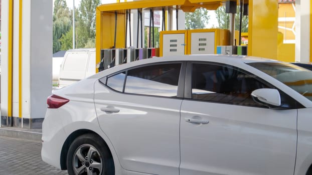 The white car is refueling. Refueling a car parked at a gas station. Refuel cars with petrol pump at gas stations. Energy of oil and gas. Fuel shortage in Ukraine. Image of pumps at a gas station