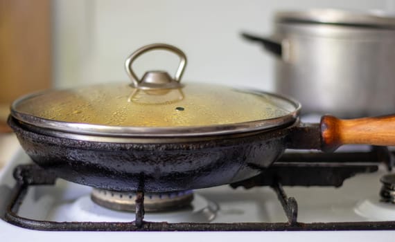Roasting fresh potatoes in a cast iron skillet with sunflower oil. A view of a stovetop with a frying pan filled with golden fried potatoes in a real kitchen. Food cooked in a homemade frying pan