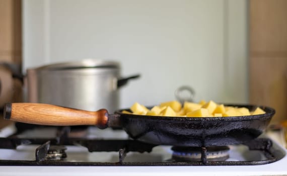 Roasting fresh potatoes in a cast iron skillet with sunflower oil. A view of a stovetop with a frying pan filled with golden fried potatoes in a real kitchen. Food cooked in a homemade frying pan