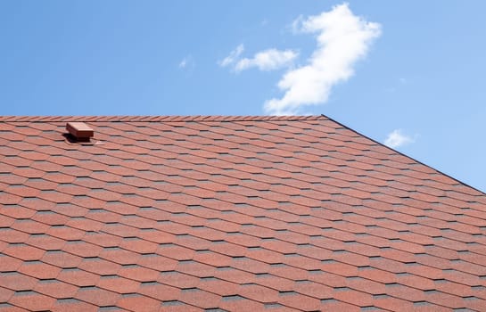 New roof with red shingles against the blue sky. High quality photo. Tiles on the roof of the house. Use to advertise roof fabrication and maintenance. Spotted texture. Affordable roofing