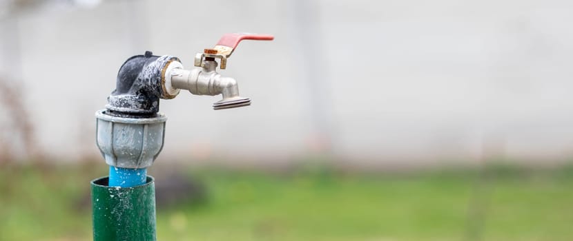 Water faucet on the background of nature. Opening or closing a faucet to save water indicates a water shortage problem. Selective focus with blurred background. Banner with copy space