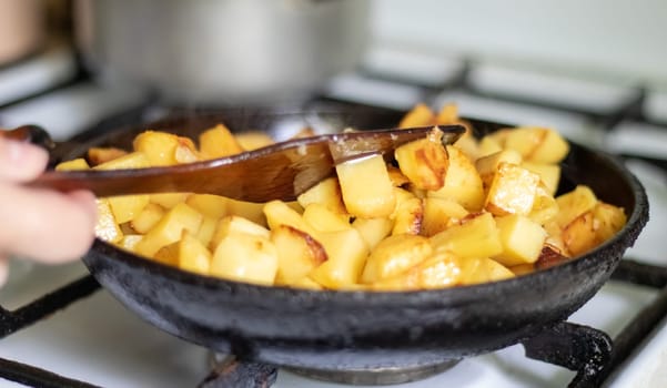 Roasting fresh potatoes in a cast iron skillet with sunflower oil. A view of a stovetop with a frying pan filled with golden fried potatoes in a real kitchen. Food cooked in a homemade frying pan