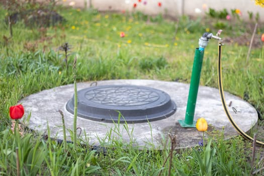 Plumbing, water pump from a well. An outside water faucet with a yellow garden hose attached to it. Irrigation water pumping system for agriculture. Hose in the garden for watering, sunny summer day
