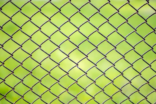 Mesh cage in the garden with green grass as background. Metal fence with wire mesh. Blurred view of the countryside through a steel iron mesh metal fence on green grass. Abstract background