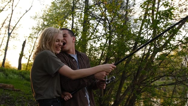 lovely young couple fishing together by a lake, river fooling and smile side shot.