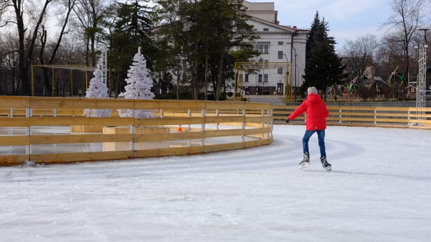 boy with red jacket, skating during the day, having fun and studying on ice rink.