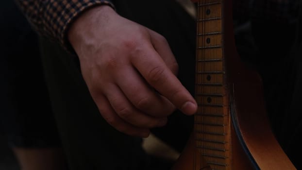 Hands of an adult man playing an acoustic guitar on the street, in a park close-up, selective focus. A man is playing an old acoustic guitar on the street. A street musician. Composer.Spanish guitar