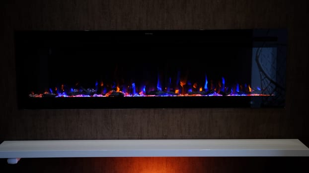 view on electric fireplace with artificial sparkling flame, decor for the interior, orange and blue flame on crystals with orange backlighting.