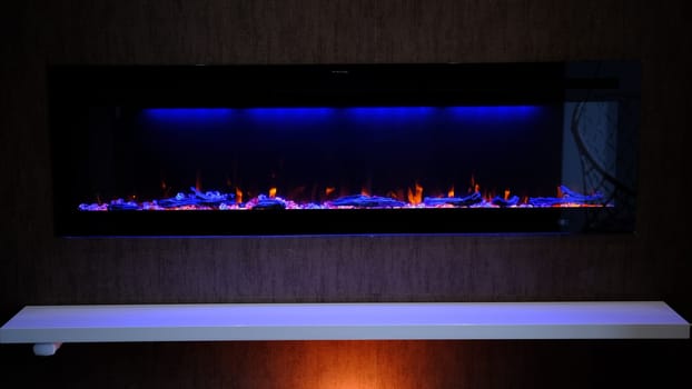 view on electric fireplace with artificial sparkling flame, decor for the interior, orange flame on crystals with blue and orange backlighting