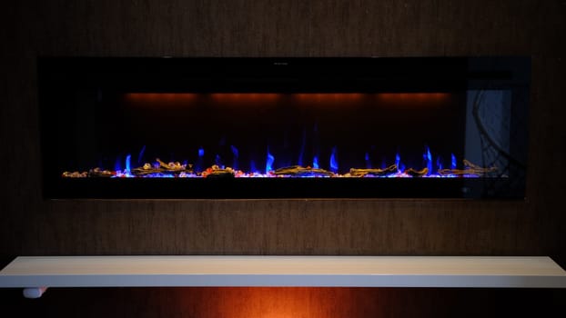 view on electric fireplace with artificial sparkling flame, decor for the interior, blue flame on crystals with orange backlighting.