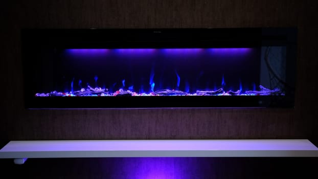 view on electric fireplace with artificial sparkling flame, decor for the interior, blue flame on crystals with violet purple backlighting.