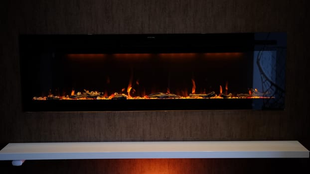view on electric fireplace with artificial sparkling flame, decor for the interior, orange flame on crystals with orange backlighting.