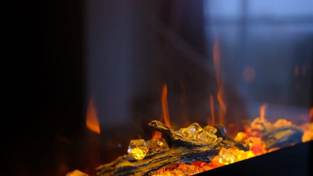 Side view on electric fireplace with artificial sparkling flame, decor for the interior, blue and orange flame with suspended swing chair in reflection.